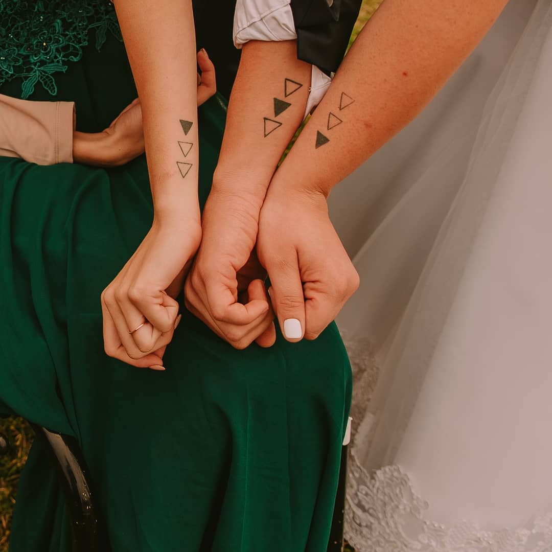 Three arms with triangle tattoos; each arm has one solid triangle